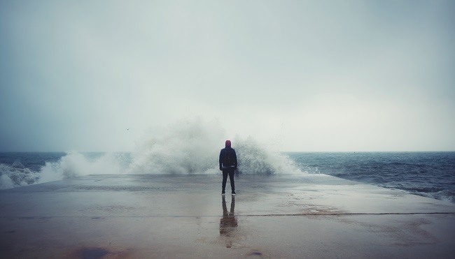 A person having an experience standing on a dock in front of a large wave.