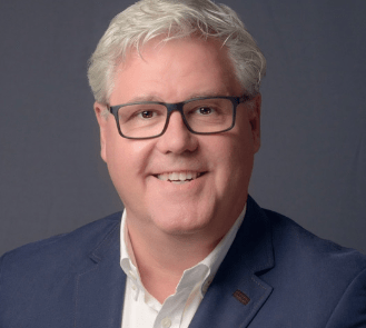 A man in glasses is confidently smiling for the camera during a sales and leadership training session.