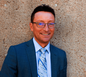 A headshot of a man in a blue suit wearing glasses